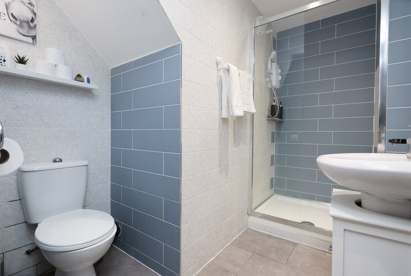 Modern bathroom with white toilet, blue subway tile walls, shower enclosure and white sink vanity