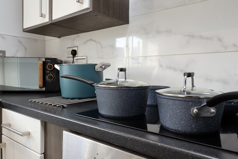 Modern kitchen stovetop with three cookpots, microwave and kitchen utensils on counter