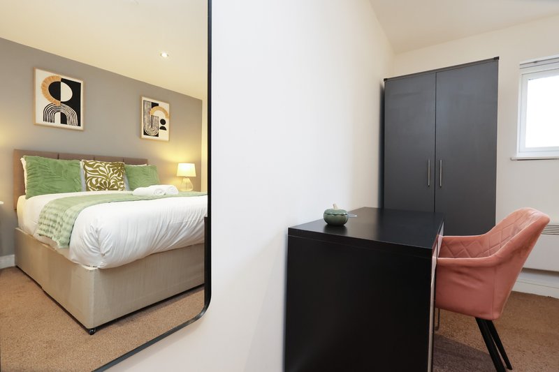 Modern bedroom with double bed, green bedding, black wardrobe and coral chair