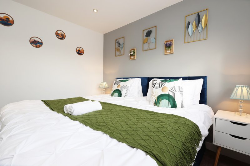Modern bedroom with double bed, green throw, white pillows and wall art