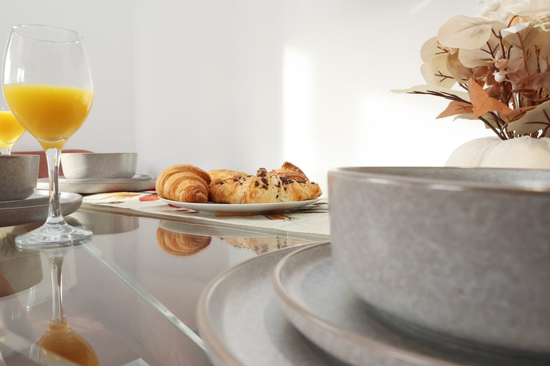 Breakfast table with orange juice, pastries, plates and flowers in natural light