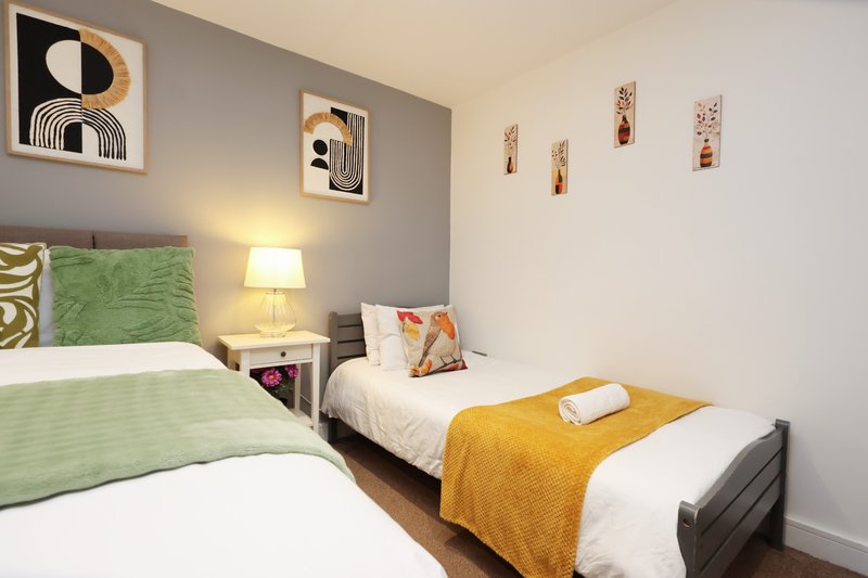 Bright bedroom with two single beds, green and yellow bedding, wall art, and bedside lamp