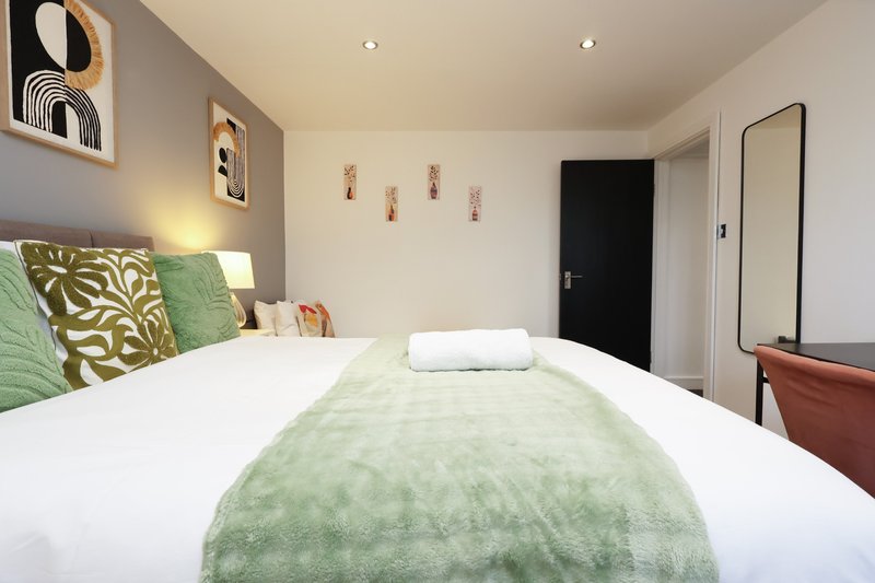Modern bedroom with double bed, green bedding, wall art, and contemporary furnishings
