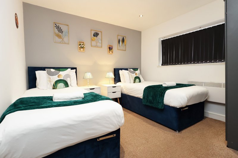 Twin bedroom with dark blue beds, white bedding, green throws, wall art and side tables