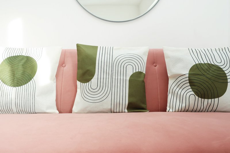 Bed with pink bedding and decorative cushions with geometric and botanical patterns