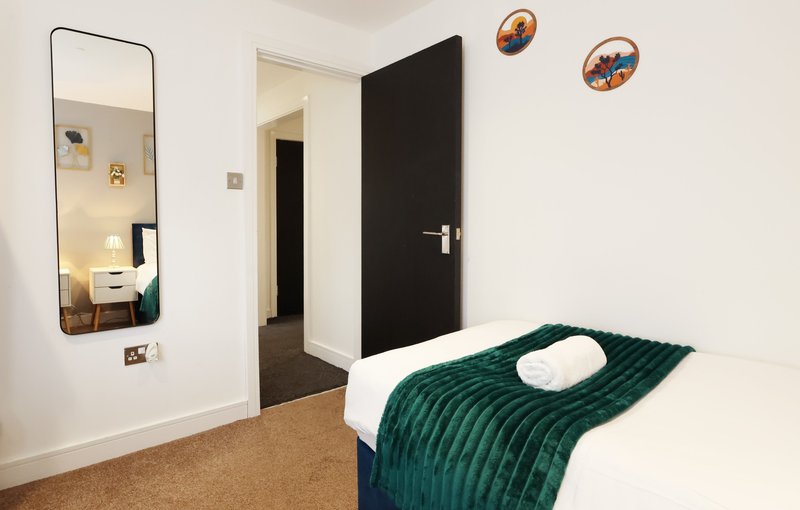 Bedroom with single bed, green blanket, mirror, black door and wall decor