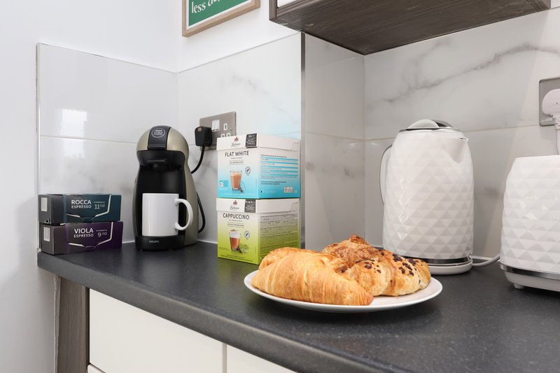 Modern kitchen counter with coffee maker, kettle, croissants on plate and branded product boxes