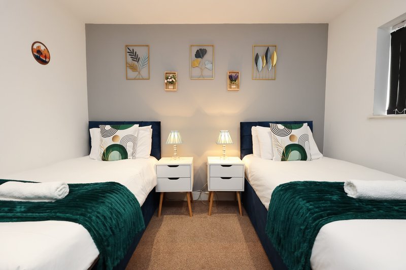 Twin bedroom with two single beds, green velvet throws, wooden bedside tables, wall art and pendant lights