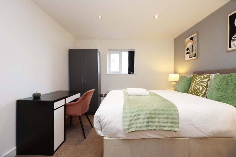 Bedroom with double bed, green bedding, desk, chair, wardrobe and window