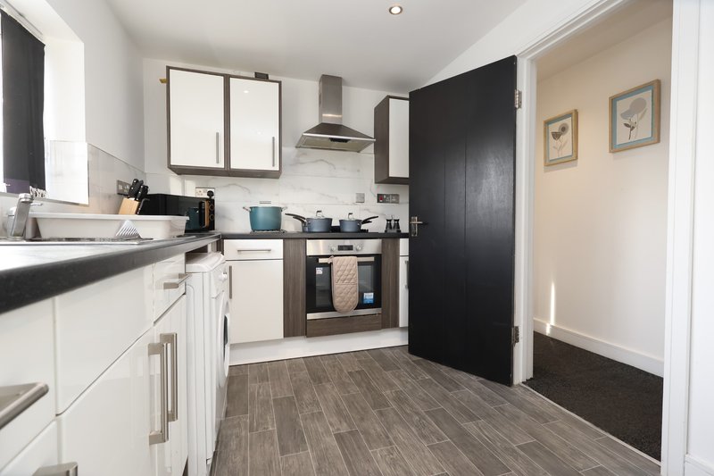 Modern kitchen with white cabinetry, black worktops, stainless steel appliances and wooden flooring