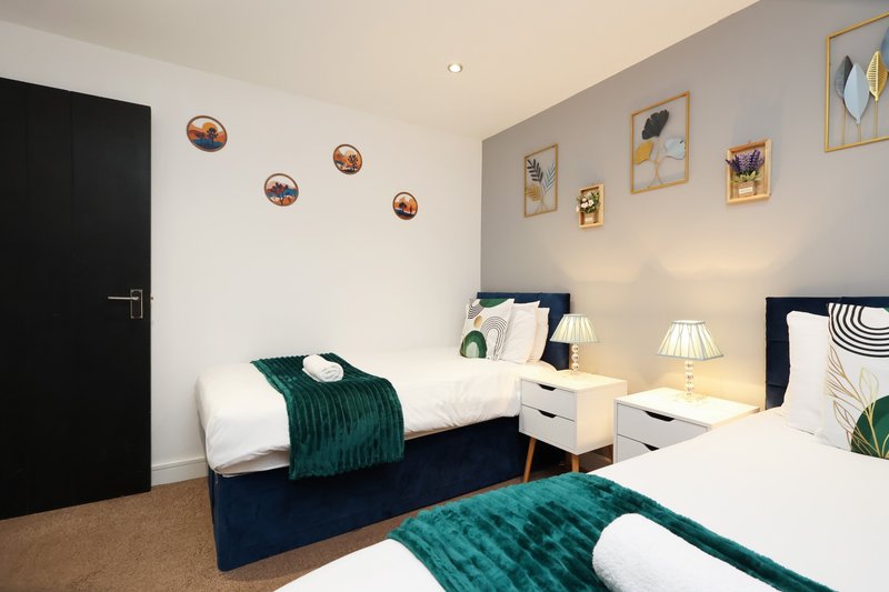 Modern bedroom with two single beds, white bedside table, wall art and teal bedding