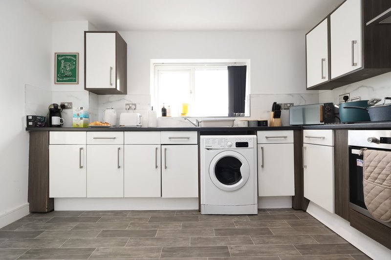 Modern kitchen with white cabinetry, integrated washing machine, and gray tile flooring