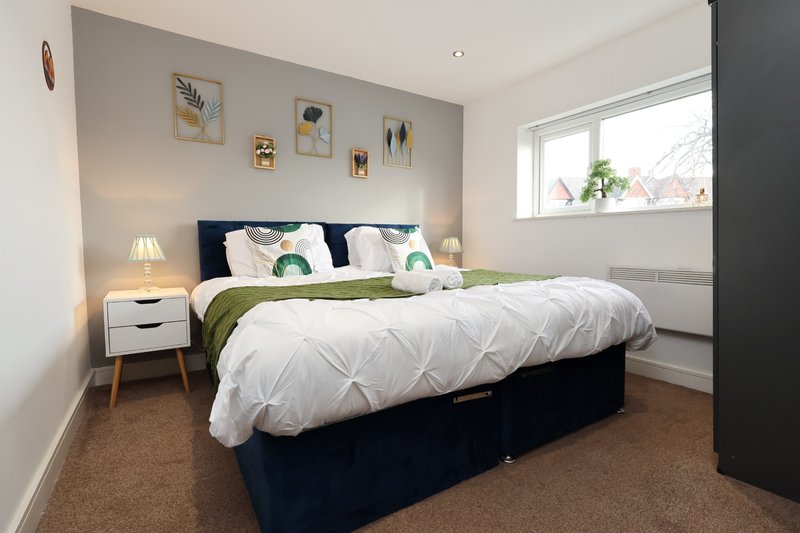 Bright modern bedroom with double bed, white duvet, navy headboard and white bedside table with lamp