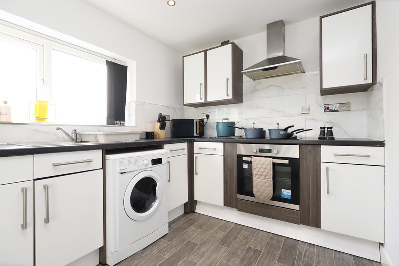 Modern kitchen with white cabinetry, black countertops, integrated appliances and wood-effect flooring