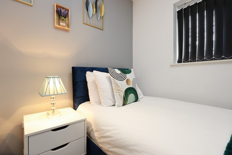 Bedroom with double bed, navy headboard, white bedding, decorative pillows, bedside lamp and nightstand