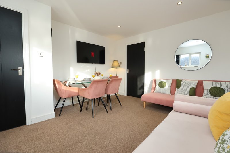 Open-plan living area with pink sofa, dining table, chairs, and mounted TV on wall
