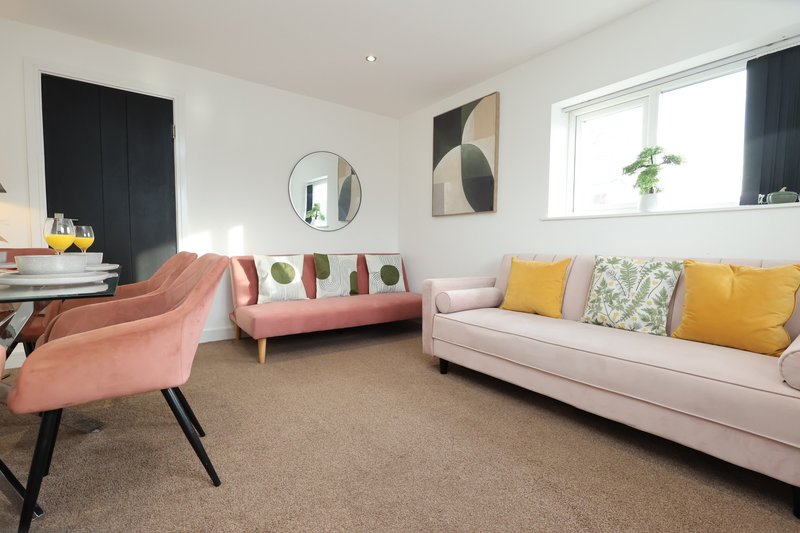 Modern living room with pink armchair, coral sofa, cream sectional, and colorful cushions
