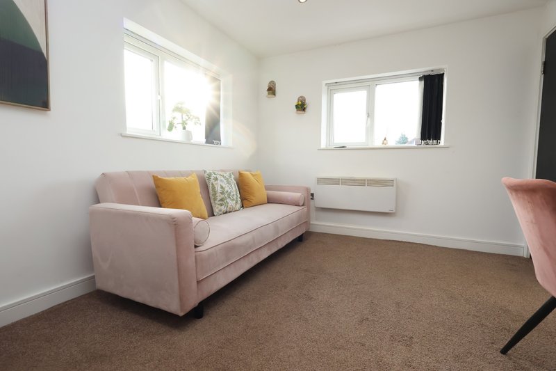 Bright living room with pink sofa, colorful cushions, two windows and brown carpet