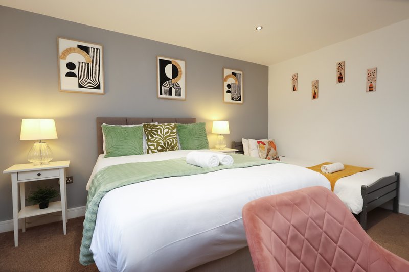Bedroom with double bed, green bedding, wall art, side lamps and pink throw