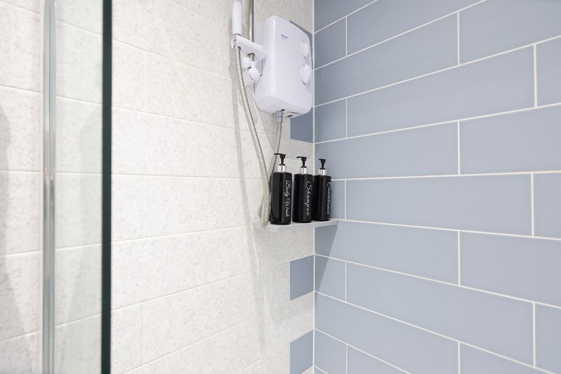 Modern bathroom with white and blue subway tile walls, shower enclosure, and toiletry bottles