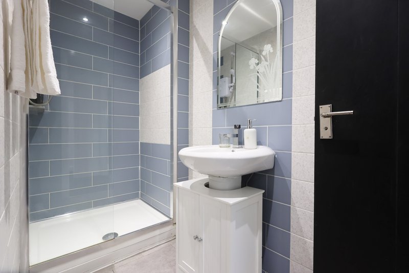 Modern bathroom with blue tile walls, walk-in shower, pedestal sink and mirror