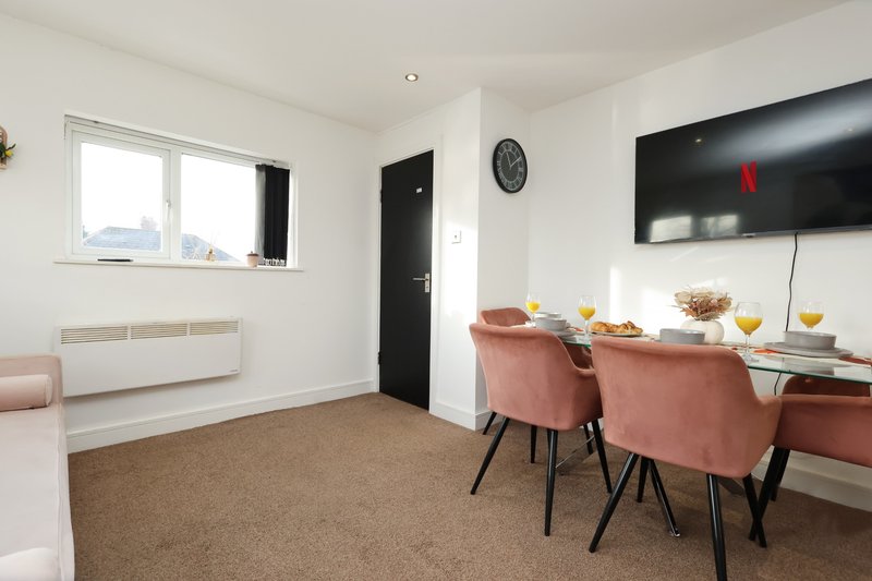 Modern open-plan living area with dining table, pink chairs, wall-mounted TV and windows