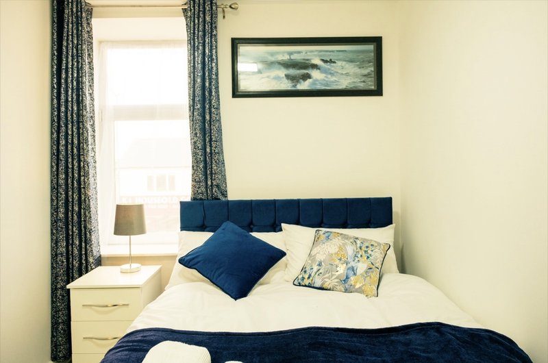 Bedroom with double bed, blue headboard, navy and white bedding, patterned cushions, bedside lamp and framed artwork