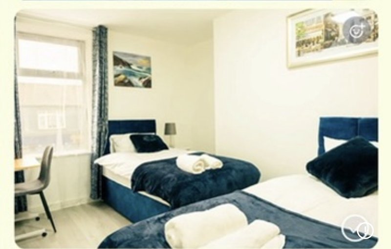 Bright bedroom with two single beds, navy blue bedding, window with curtains, desk chair