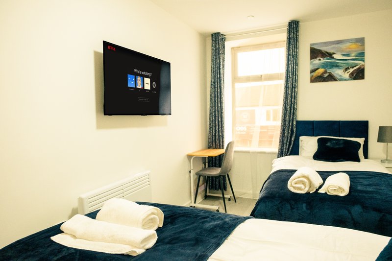 Bright modern bedroom with two single beds, wall-mounted TV, window with curtains and folded towels