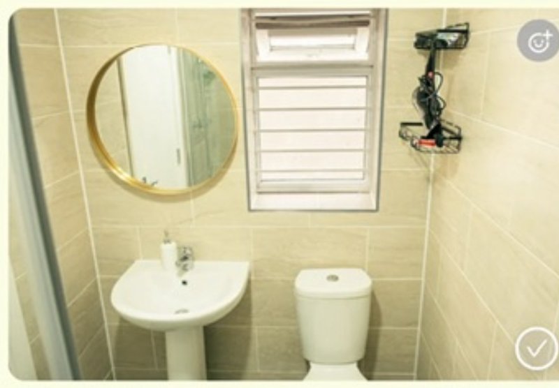 Small bathroom with pedestal sink, toilet, round mirror and window