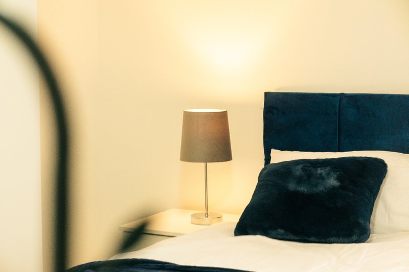 Modern bedroom with dark headboard, black fur cushion, bedside lamp and cream walls