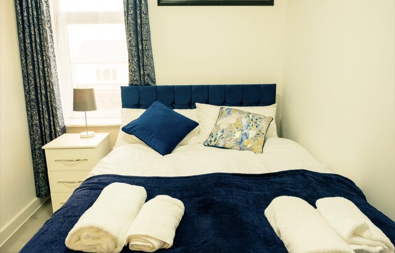 Bedroom with double bed, navy headboard, blue bedding, cream pillows and folded towels