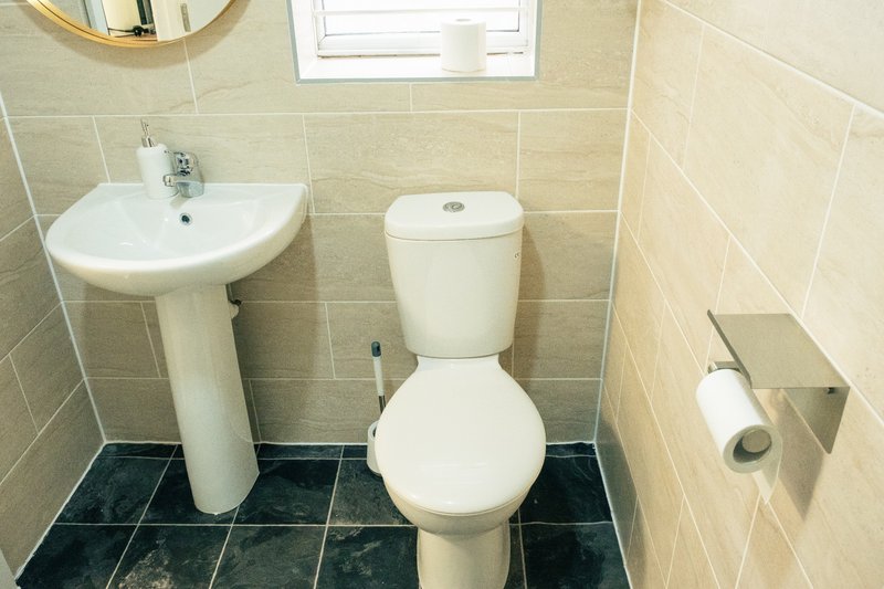 Small bathroom with pedestal sink, toilet, window and dark tile flooring