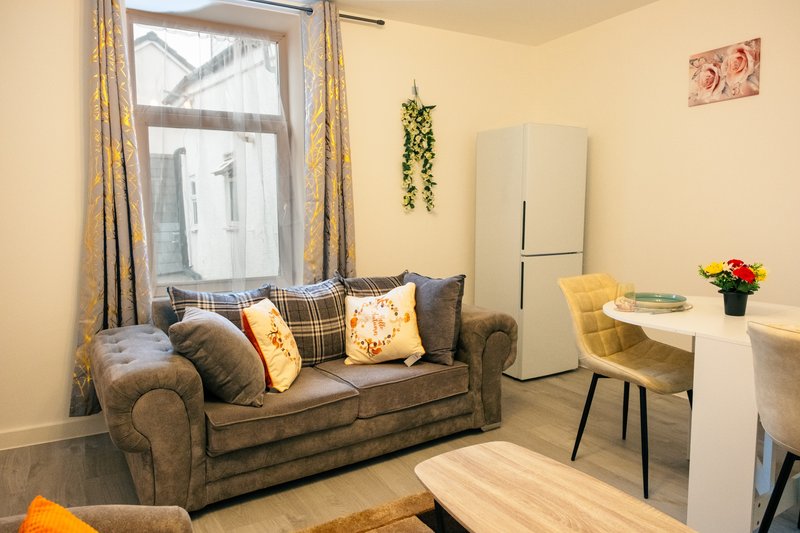 Living room with grey sofa, patterned cushions, window with curtains, small desk and chair