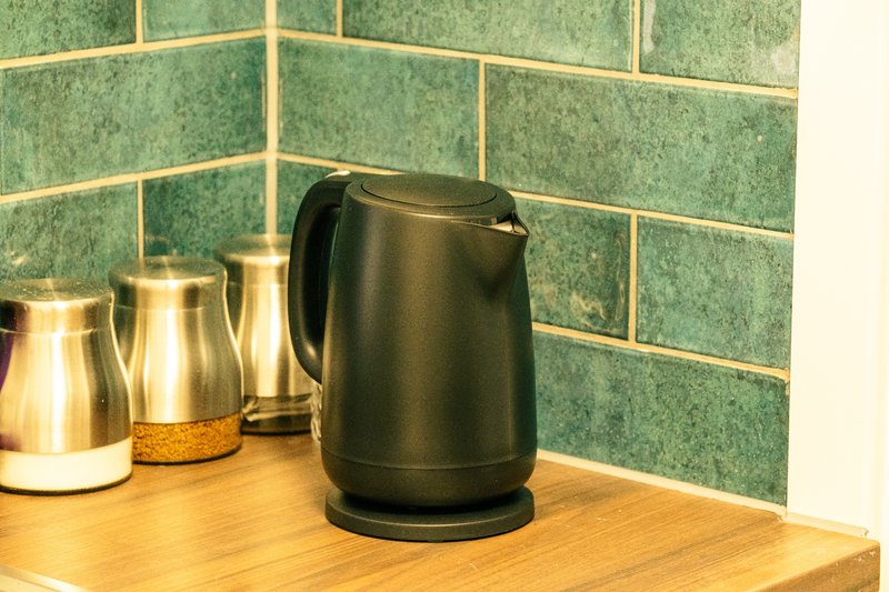 Kitchen counter with black electric kettle and stainless steel thermal jugs against green subway tile