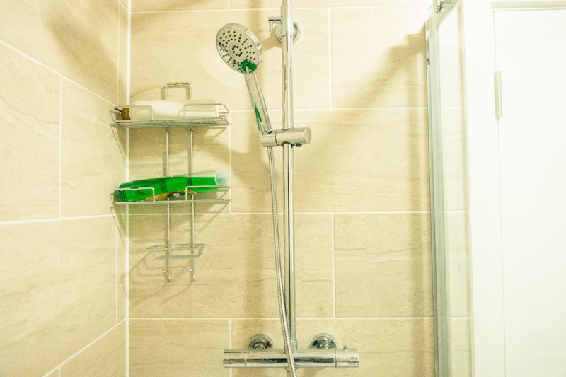Modern shower enclosure with cream tile walls, rainfall showerhead, and chrome fixtures