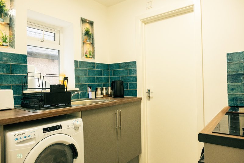 Bathroom with teal tile walls, wooden countertop, washing machine and sink