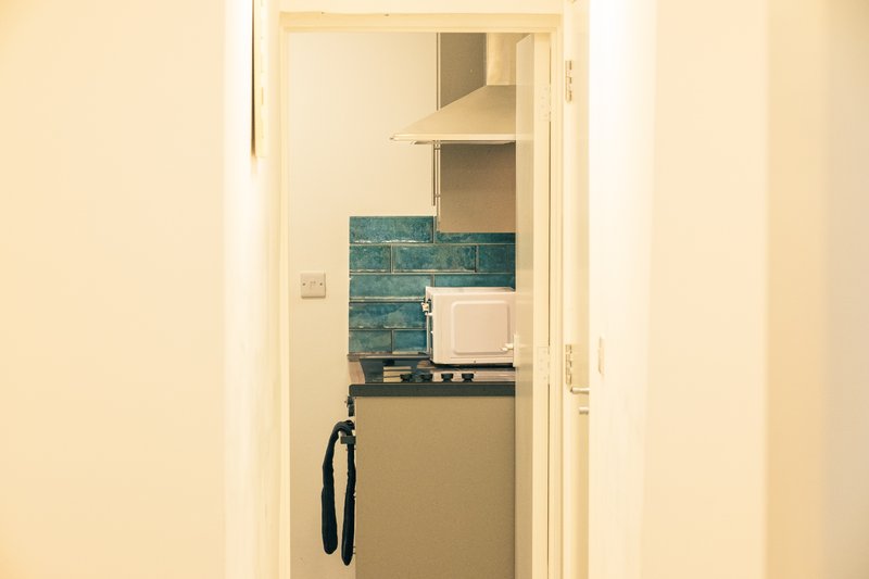 Kitchen alcove with teal tile backsplash, white cabinetry, and cooking appliances visible through doorway
