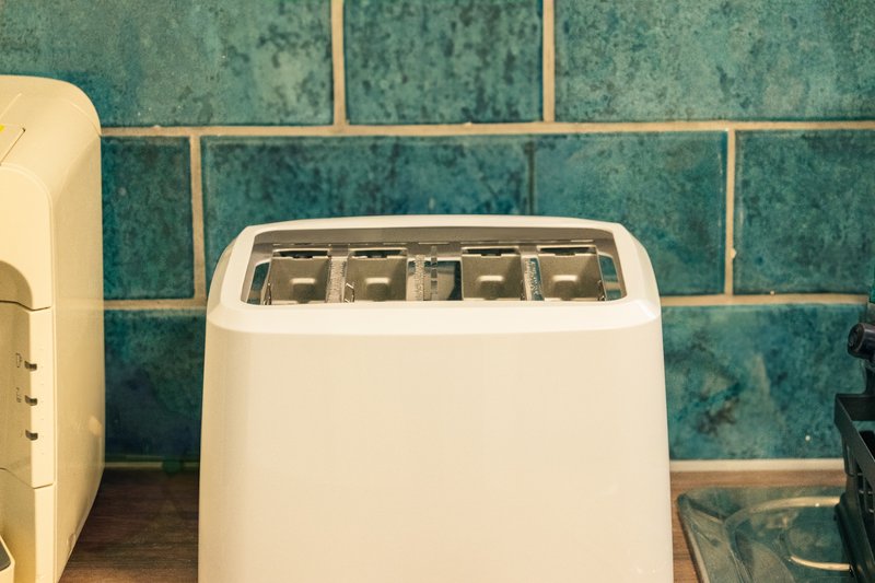 White toaster on kitchen counter with teal tile backsplash and cream kettle
