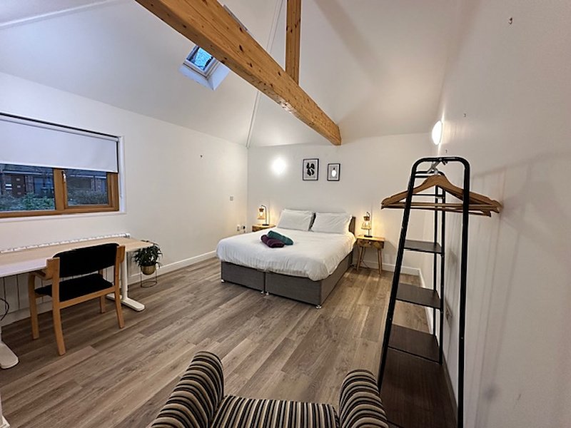 Modern bedroom with double bed, wooden beams, desk area, and striped rug