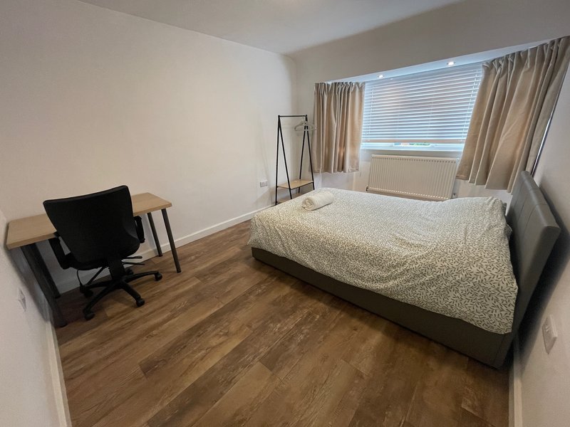 Bedroom with double bed, desk chair, wooden floor and window with blinds