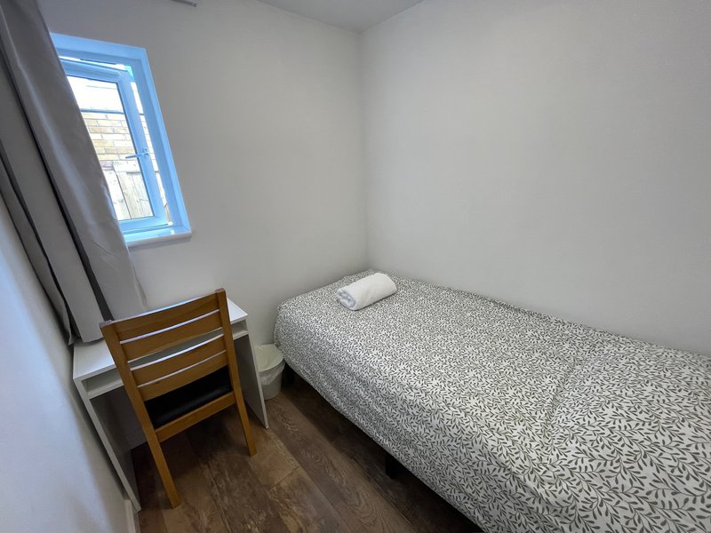 Compact bedroom with single bed, wooden chair, small window and wooden flooring