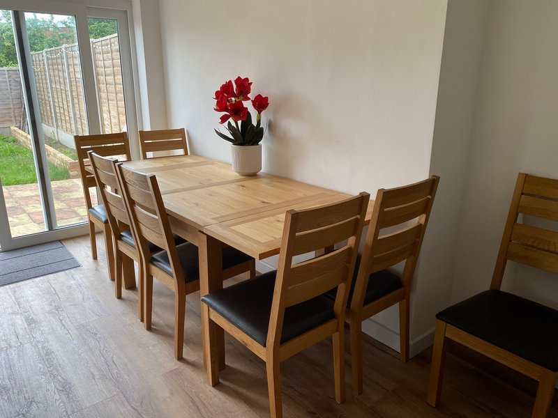 Dining room with wooden table, six chairs, red flowers in vase, garden view through doors
