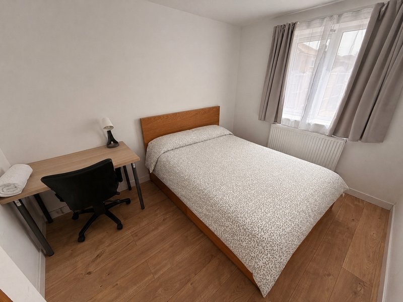 Bright bedroom with double bed, wooden desk, office chair and window with curtains