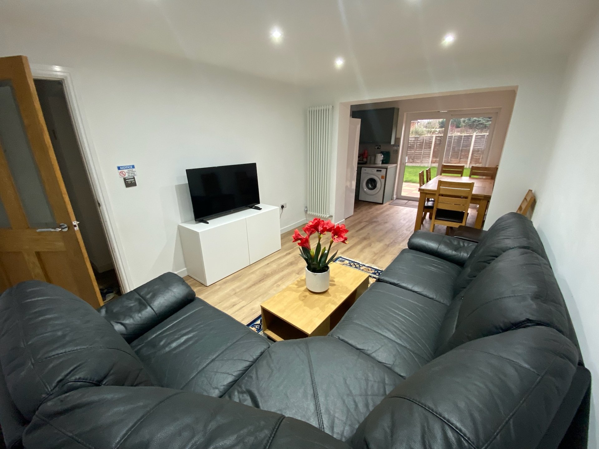 Open-plan living room with black leather sofa, TV, wooden coffee table and flowers