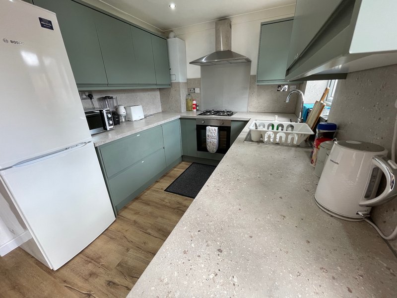 Modern kitchen with sage green cabinetry, white appliances, gas hob and stainless steel extractor hood