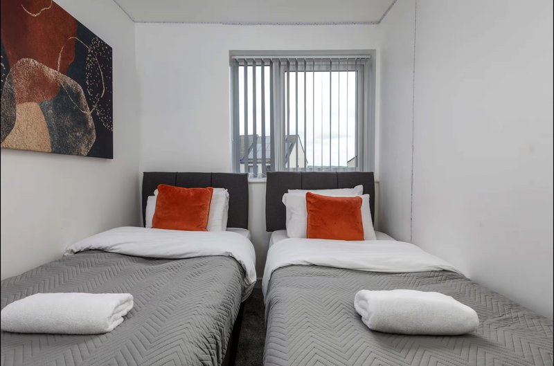 Twin bedroom with two single beds, white pillows, orange cushions, grey bedding and window
