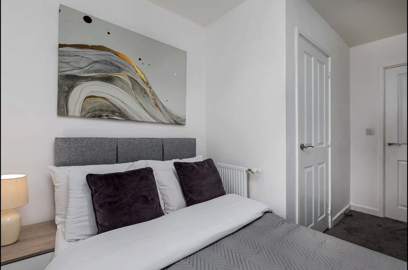 Modern bedroom with double bed, gray headboard, dark cushions, and abstract wall art
