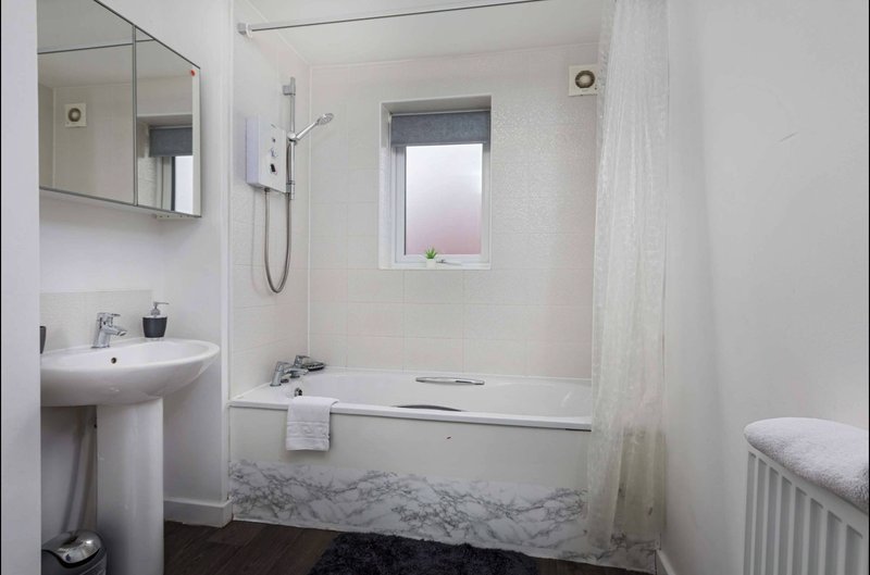 Clean modern bathroom with pedestal sink, shower enclosure, window and radiator