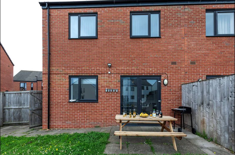 Red brick semi-detached house exterior with patio, wooden picnic table and green lawn